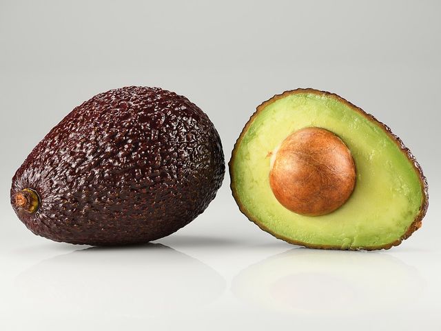 Aguacate Hass entero junto a una mitad con la semilla